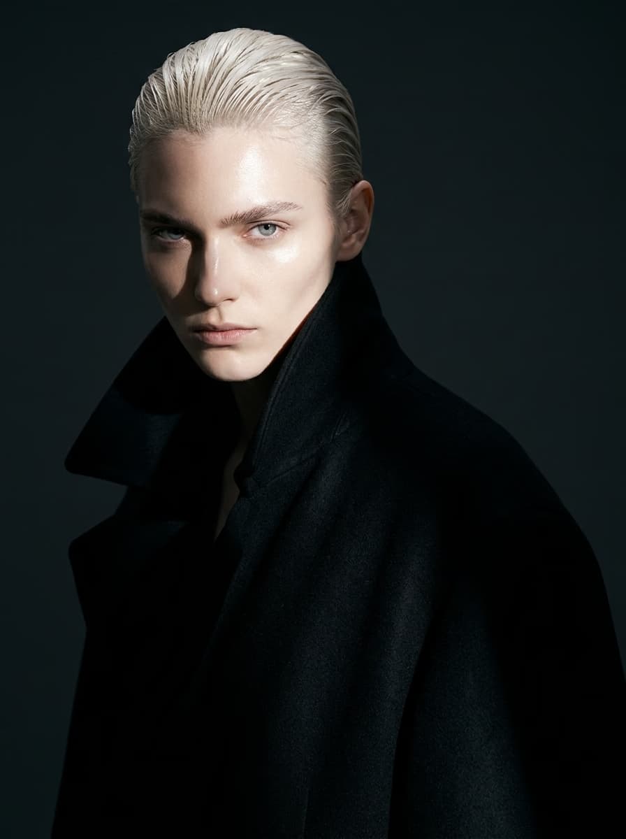 Editorial studio portrait of a persona with platinum hair in a black coat